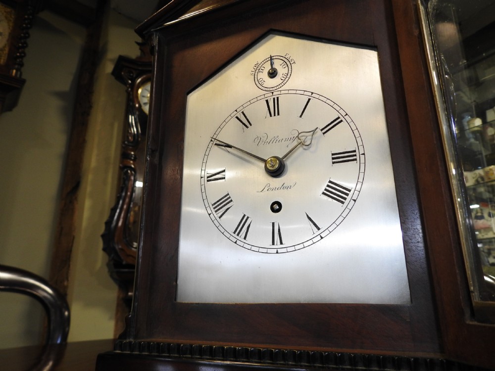 An antique Regency flame mahogany bracket clock featuring a gabled top, a silvered dial signed Vulliamy London, and brass ball feet. View V