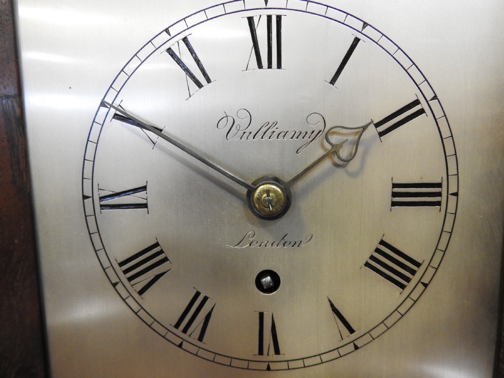 An antique Regency flame mahogany bracket clock featuring a gabled top, a silvered dial signed Vulliamy London, and brass ball feet. View VII