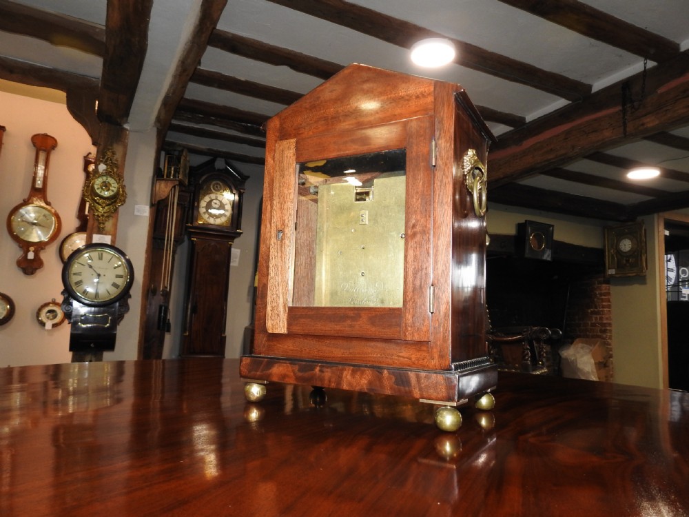 An antique Regency flame mahogany bracket clock featuring a gabled top, a silvered dial signed Vulliamy London, and brass ball feet. View XVI