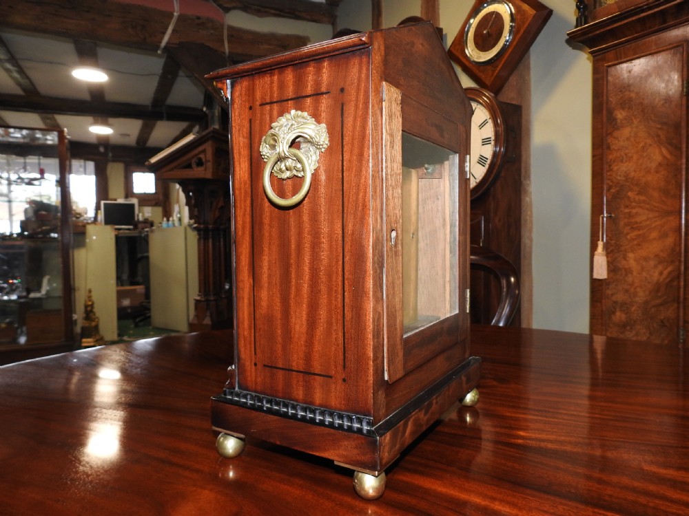An antique Regency flame mahogany bracket clock featuring a gabled top, a silvered dial signed Vulliamy London, and brass ball feet. View XVII