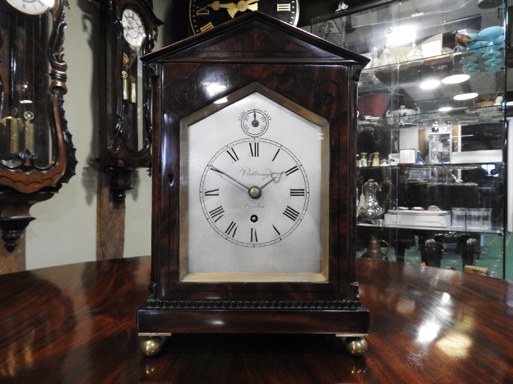 An antique Regency flame mahogany bracket clock featuring a gabled top, a silvered dial signed Vulliamy London, and brass ball feet. View XIX