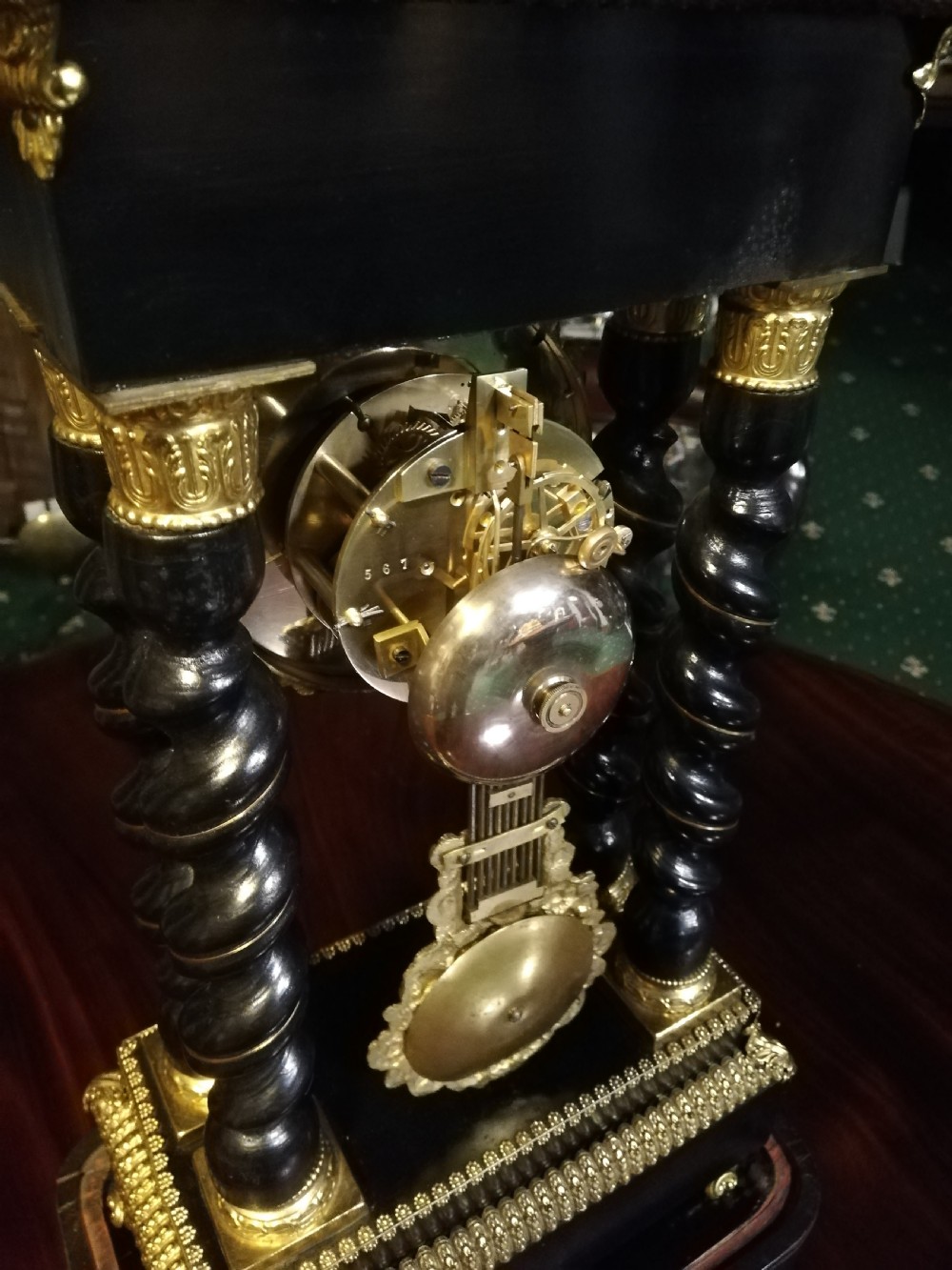 A 19th-century French portico mantel clock featuring ebonised barley twist columns, gilt bronze mounts, stone inlay, and an original glass cloche. View XIV