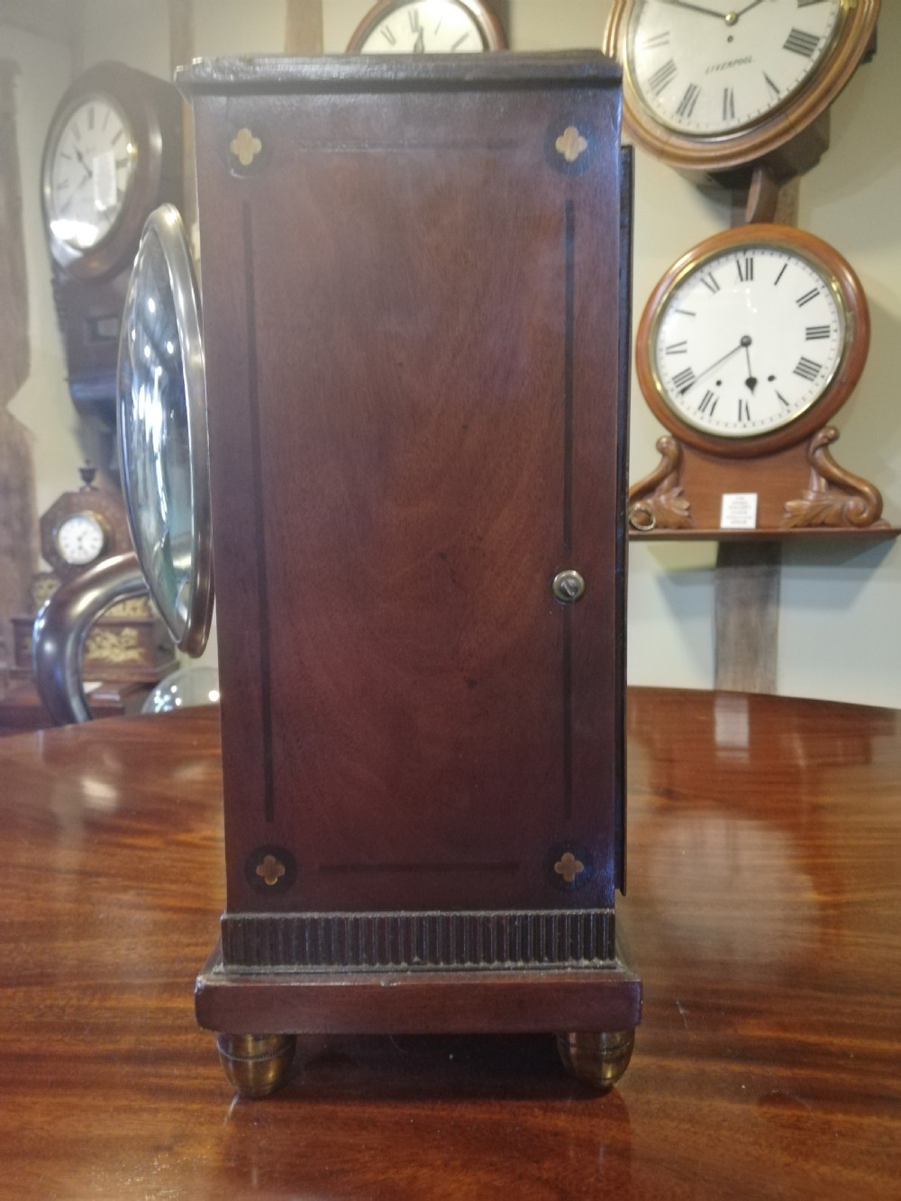 An antique mahogany bracket clock featuring an arched top, inlaid woodwork, a white dial with Roman numerals signed W. Clark London, and brass bun feet. View VI