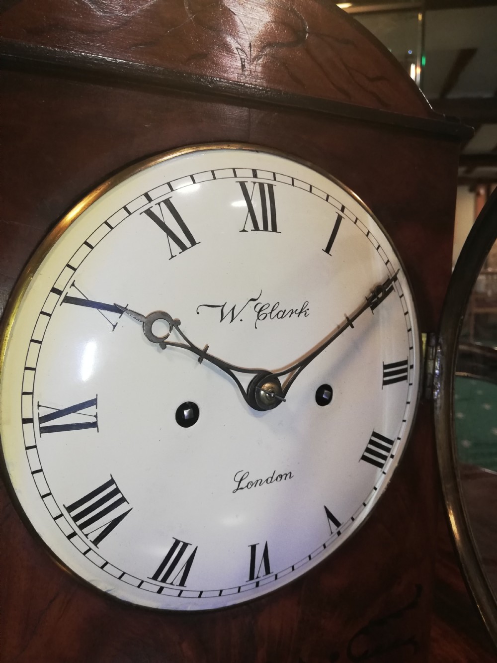 An antique mahogany bracket clock featuring an arched top, inlaid woodwork, a white dial with Roman numerals signed W. Clark London, and brass bun feet. View VII