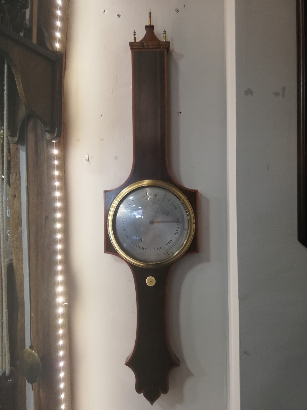 An antique Georgian mahogany wheel barometer featuring a silvered dial with brass bezel, dark wooden casing with inlay, and a pediment top. View VIII