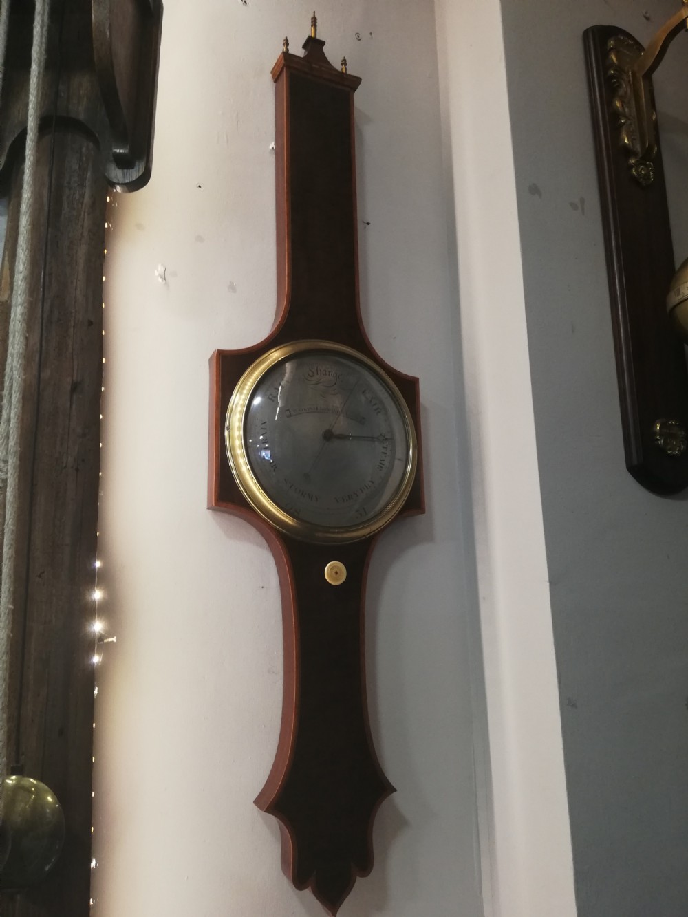An antique Georgian mahogany wheel barometer featuring a silvered dial with brass bezel, dark wooden casing with inlay, and a pediment top. View II