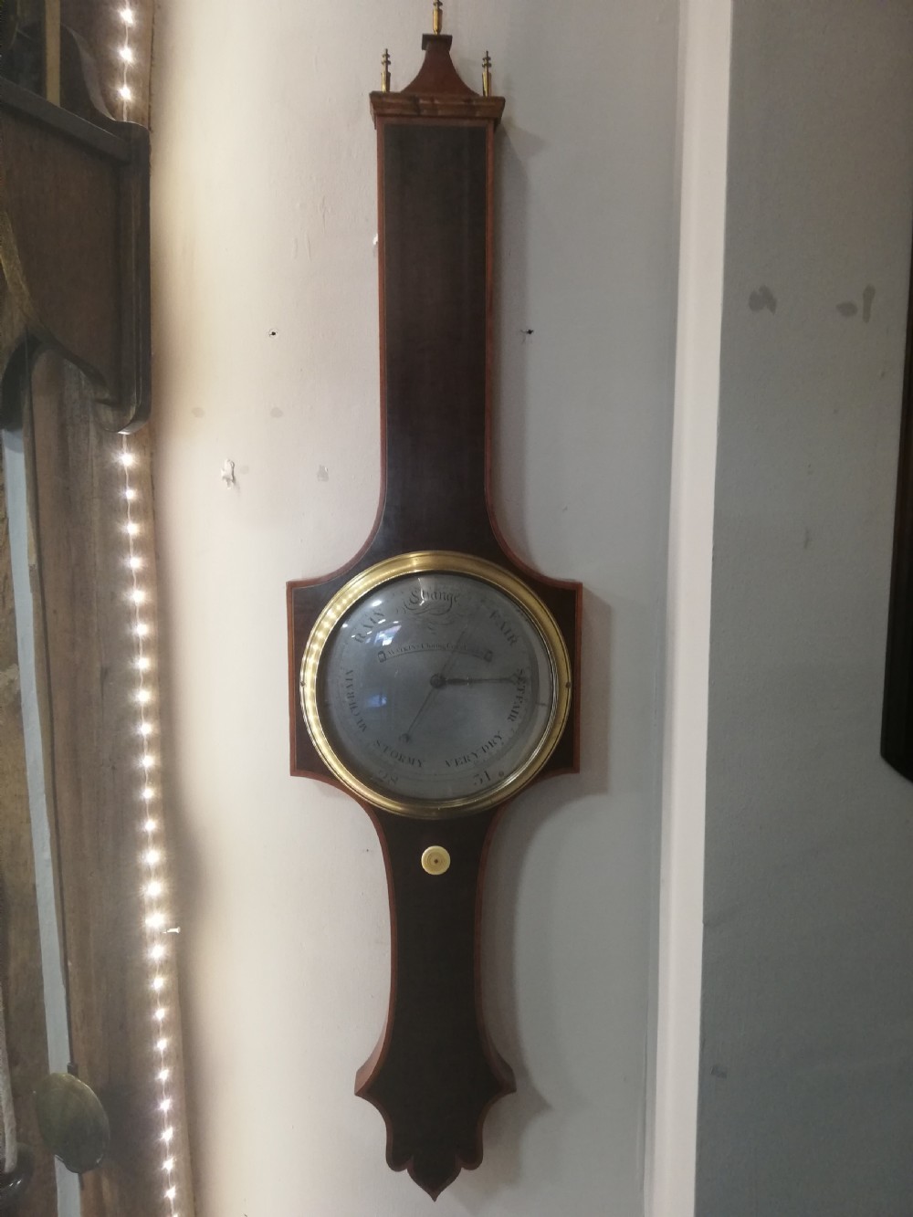 An antique Georgian mahogany wheel barometer featuring a silvered dial with brass bezel, dark wooden casing with inlay, and a pediment top. View III