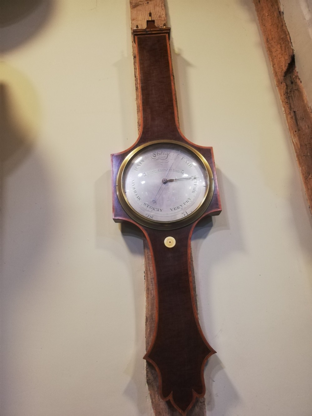 An antique Georgian mahogany wheel barometer featuring a silvered dial with brass bezel, dark wooden casing with inlay, and a pediment top. View IV