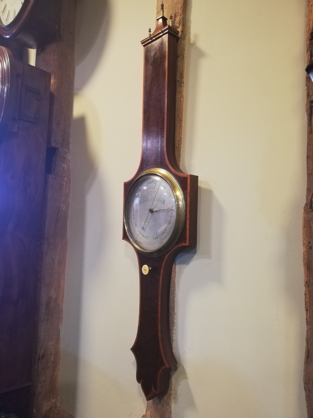 An antique Georgian mahogany wheel barometer featuring a silvered dial with brass bezel, dark wooden casing with inlay, and a pediment top. View V