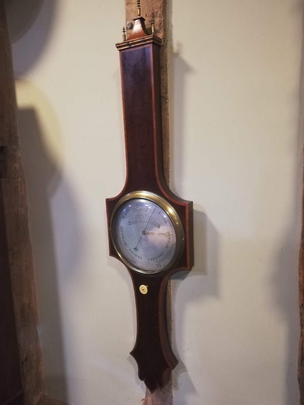 An antique Georgian mahogany wheel barometer featuring a silvered dial with brass bezel, dark wooden casing with inlay, and a pediment top. View VI