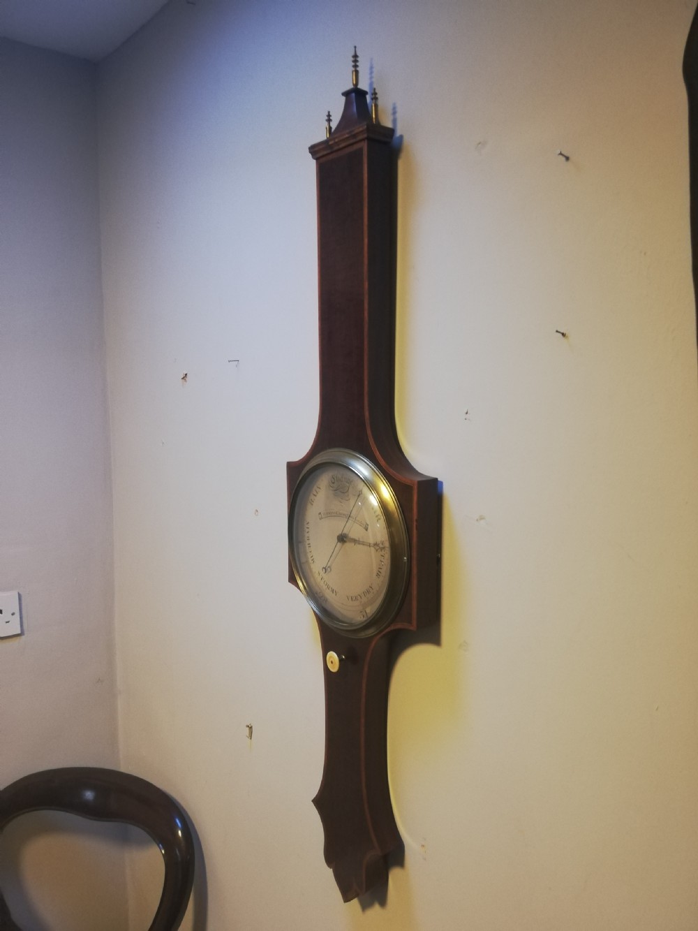 An antique Georgian mahogany wheel barometer featuring a silvered dial with brass bezel, dark wooden casing with inlay, and a pediment top. View IX