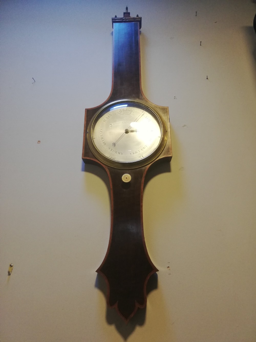 An antique Georgian mahogany wheel barometer featuring a silvered dial with brass bezel, dark wooden casing with inlay, and a pediment top. View XV