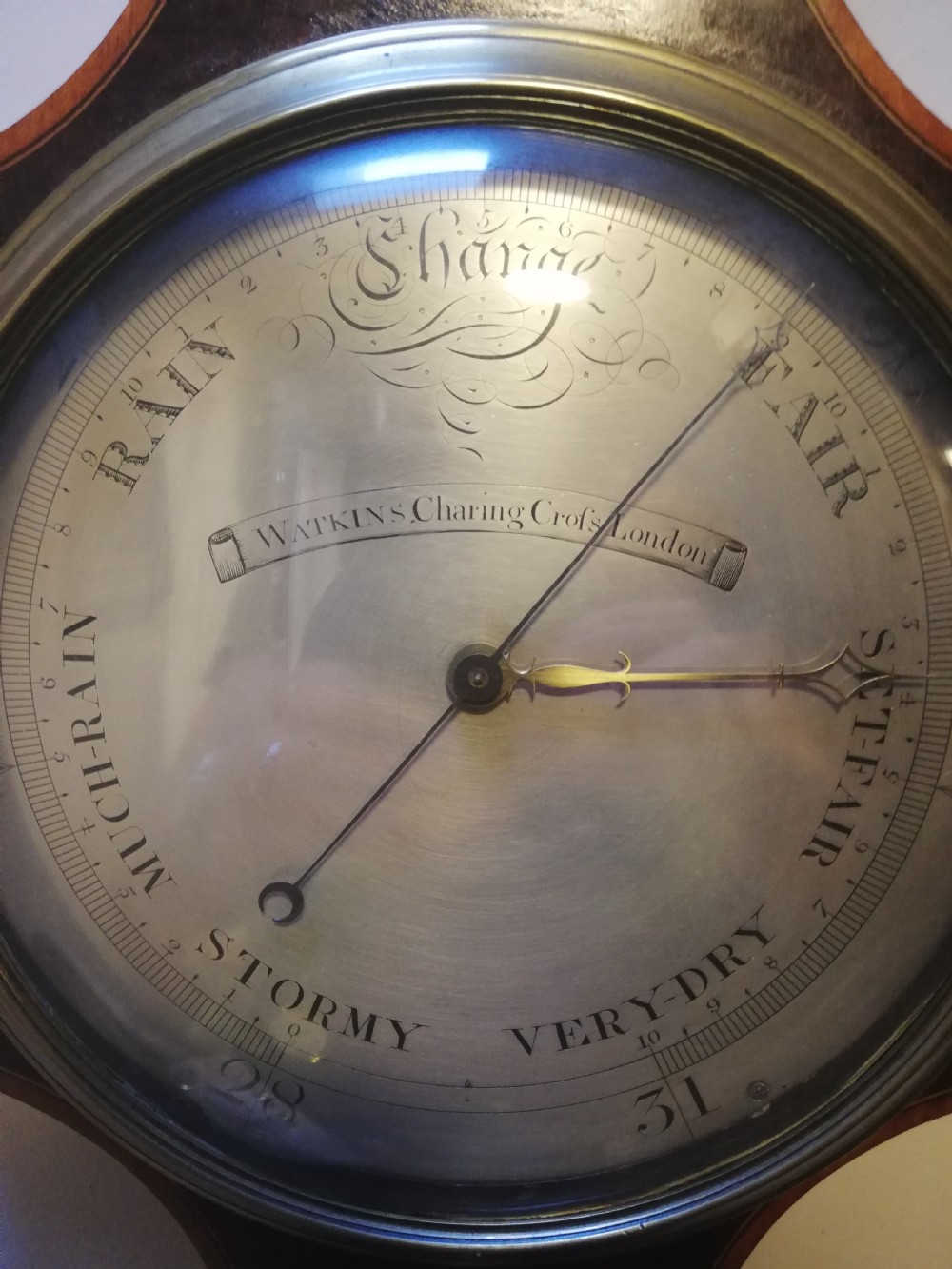 An antique Georgian mahogany wheel barometer featuring a silvered dial with brass bezel, dark wooden casing with inlay, and a pediment top. View XVI