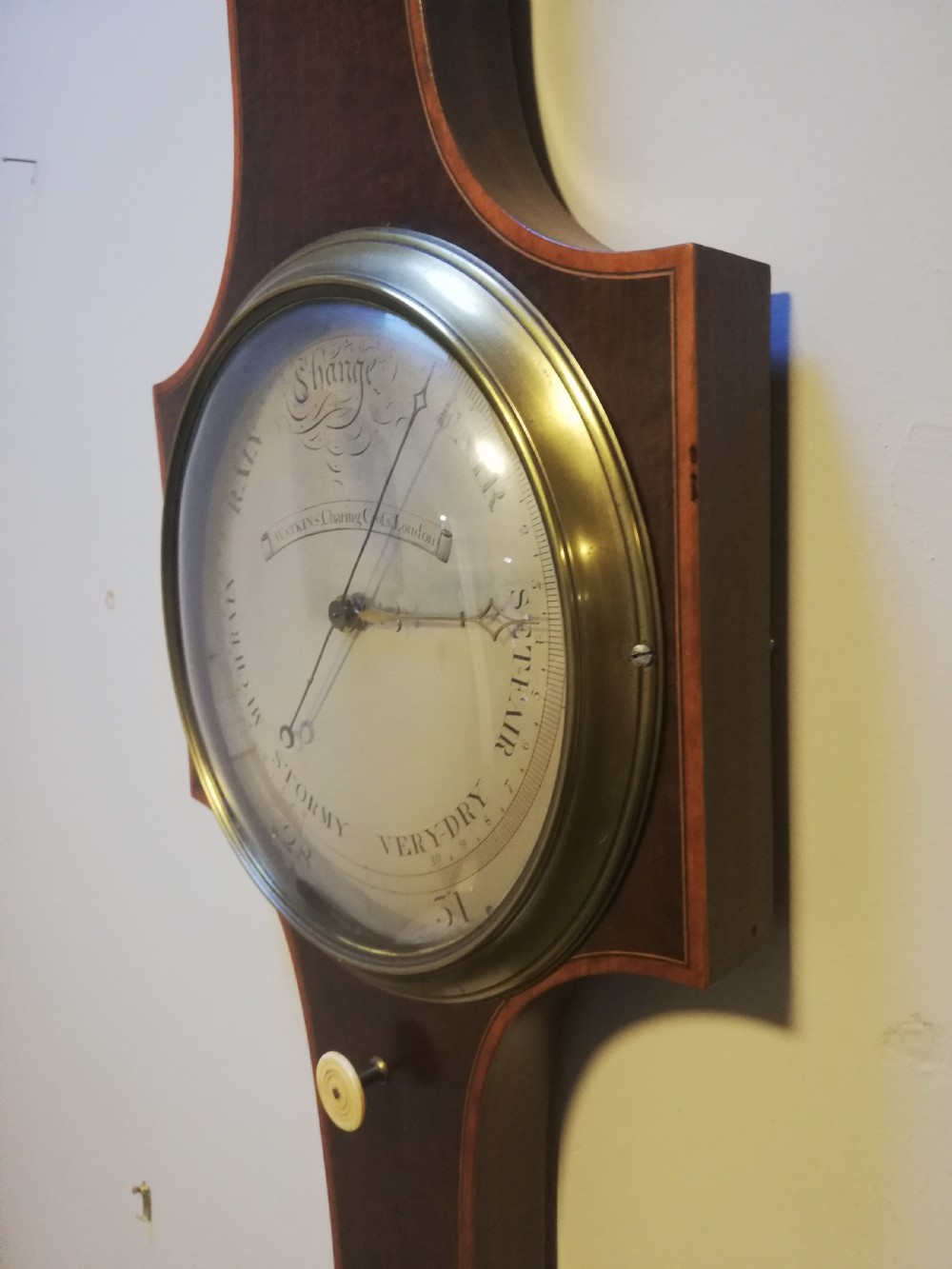 An antique Georgian mahogany wheel barometer featuring a silvered dial with brass bezel, dark wooden casing with inlay, and a pediment top. View XVII