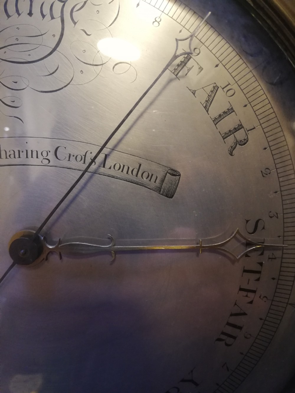 An antique Georgian mahogany wheel barometer featuring a silvered dial with brass bezel, dark wooden casing with inlay, and a pediment top. View XXIV
