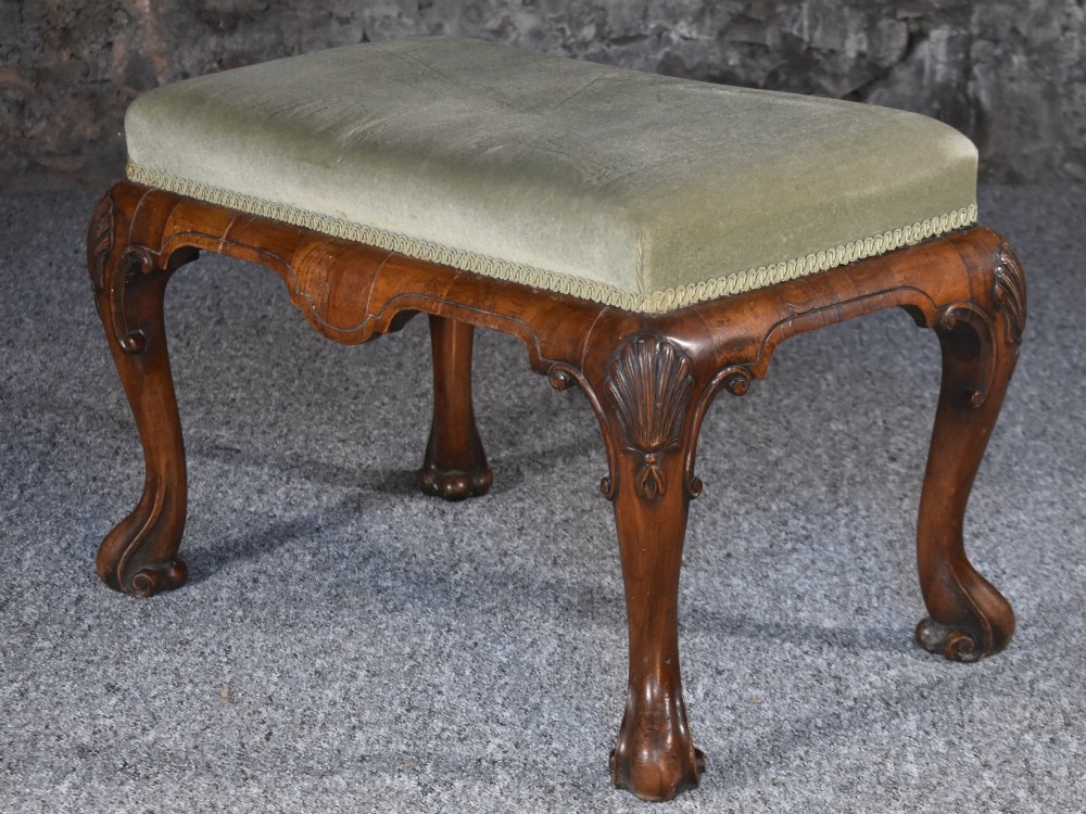 A rectangular George I style walnut stool featuring carved cabriole legs with shell motifs and a sage green velvet seat.