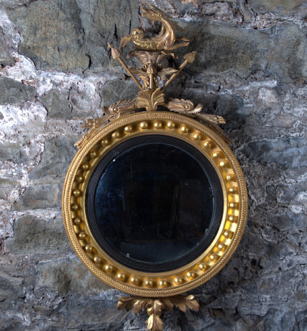 A circular Regency giltwood convex mirror featuring a carved dragon crest atop a moulded frame adorned with spherules and an acanthus leaf base pendant.