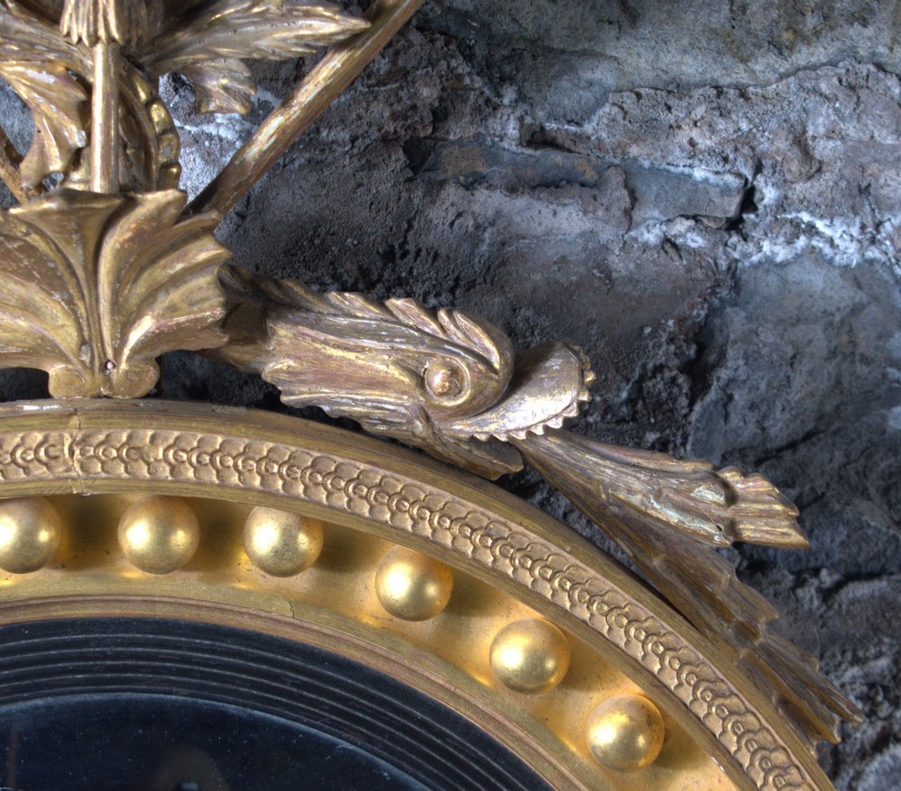 A circular Regency giltwood convex mirror featuring a carved dragon crest atop a moulded frame adorned with spherules and an acanthus leaf base pendant. View II