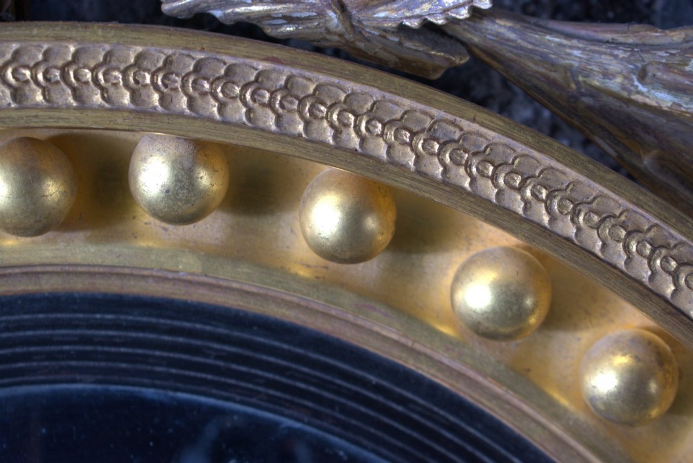 A circular Regency giltwood convex mirror featuring a carved dragon crest atop a moulded frame adorned with spherules and an acanthus leaf base pendant. View IV