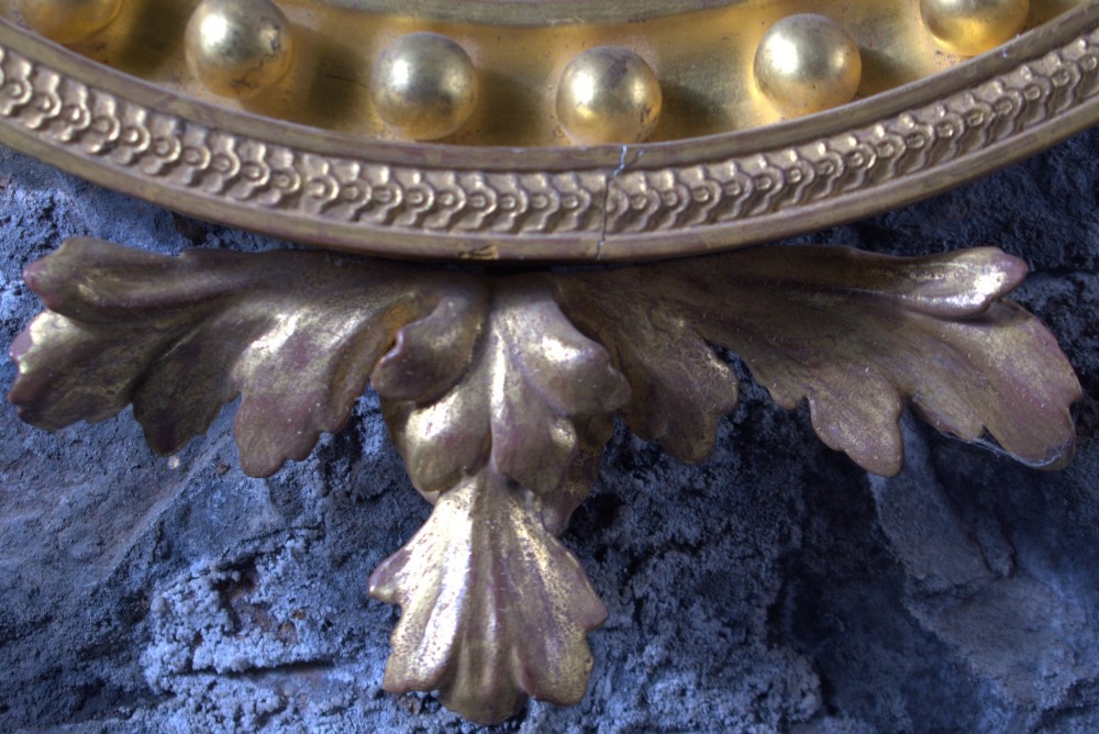A circular Regency giltwood convex mirror featuring a carved dragon crest atop a moulded frame adorned with spherules and an acanthus leaf base pendant. View V
