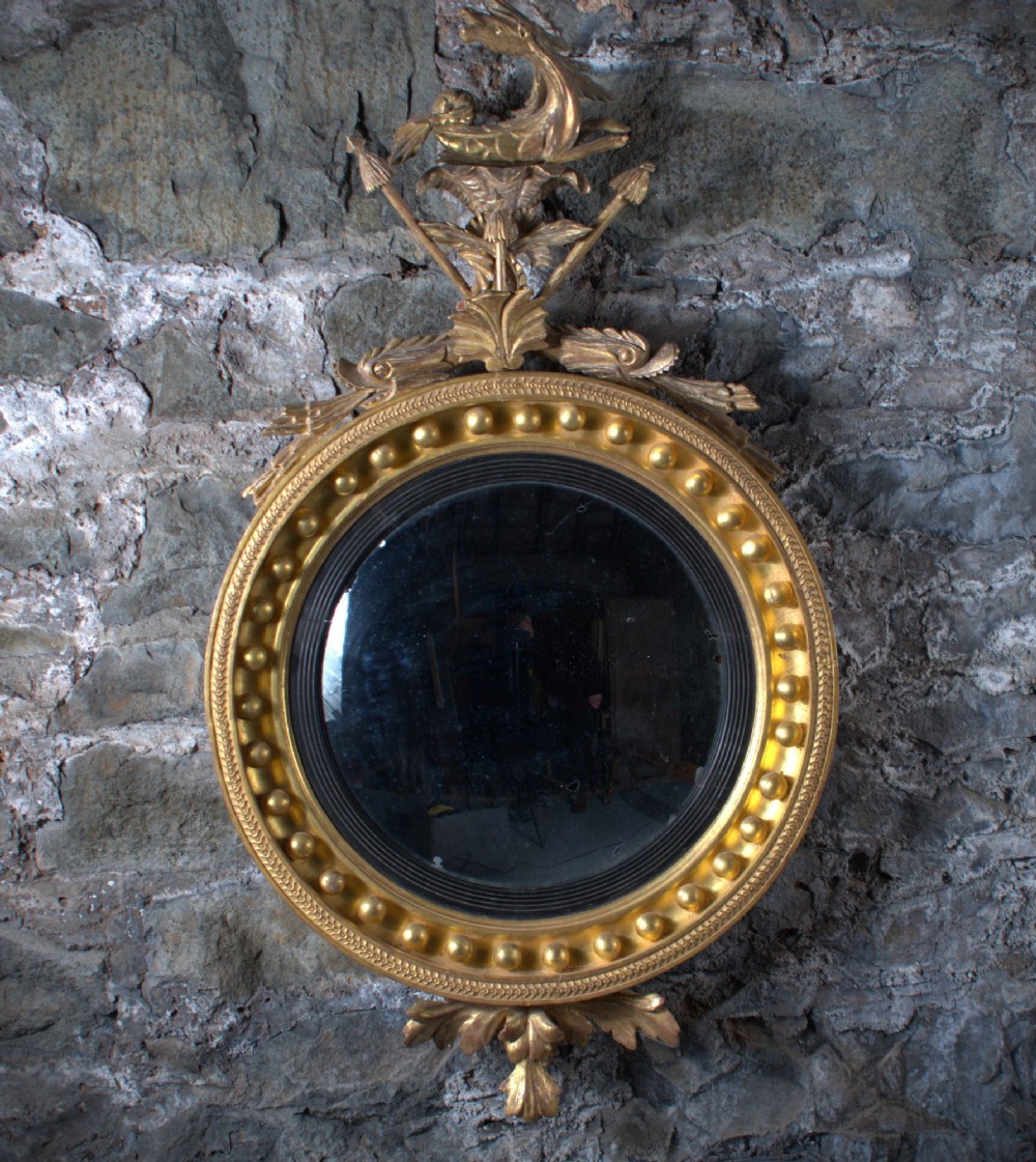 A circular Regency giltwood convex mirror featuring a carved dragon crest atop a moulded frame adorned with spherules and an acanthus leaf base pendant. View VII