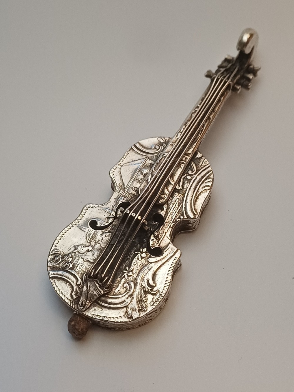 A miniature 19th-century Dutch silver scent bottle crafted in the shape of a violin with engraved scenes and silver wire strings.