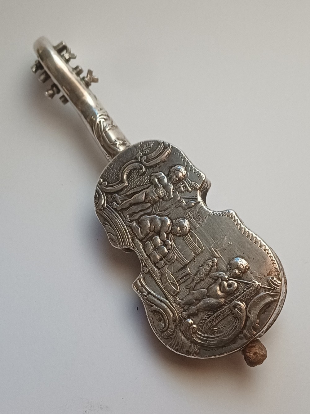A miniature 19th-century Dutch silver scent bottle crafted in the shape of a violin with engraved scenes and silver wire strings. View II