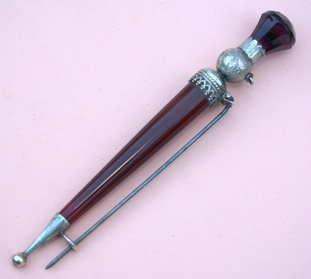 A Victorian Scottish silver and red agate dirk brooch shaped like a dagger with engraved thistle details and a faceted purple stone pommel.