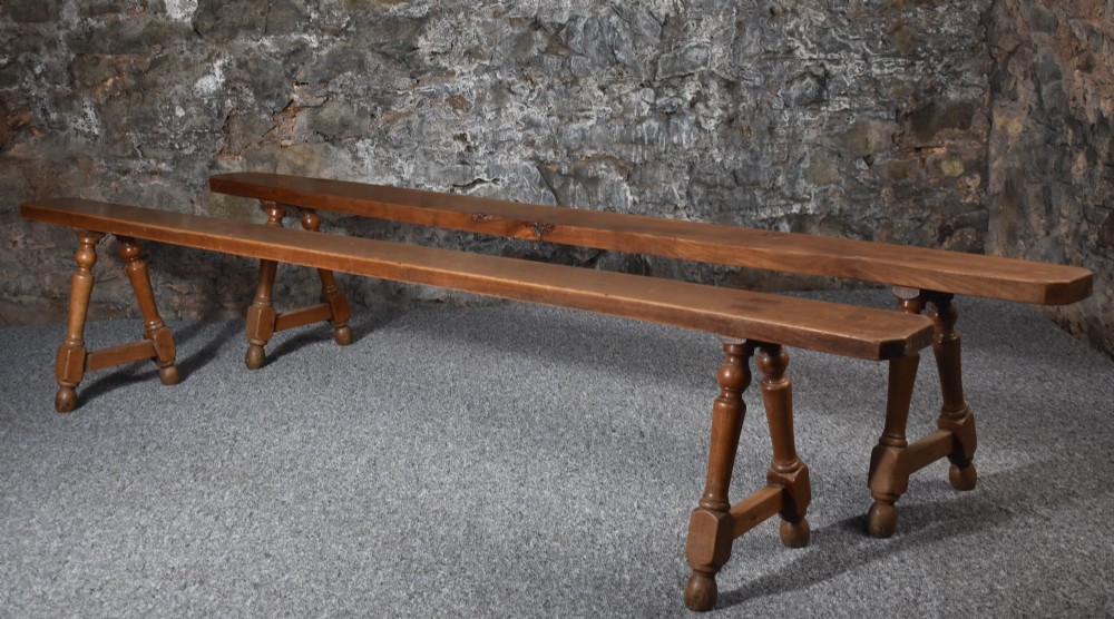 A pair of long 19th-century cherry wood benches with turned trestle legs, stretchers, and smooth timber tops.