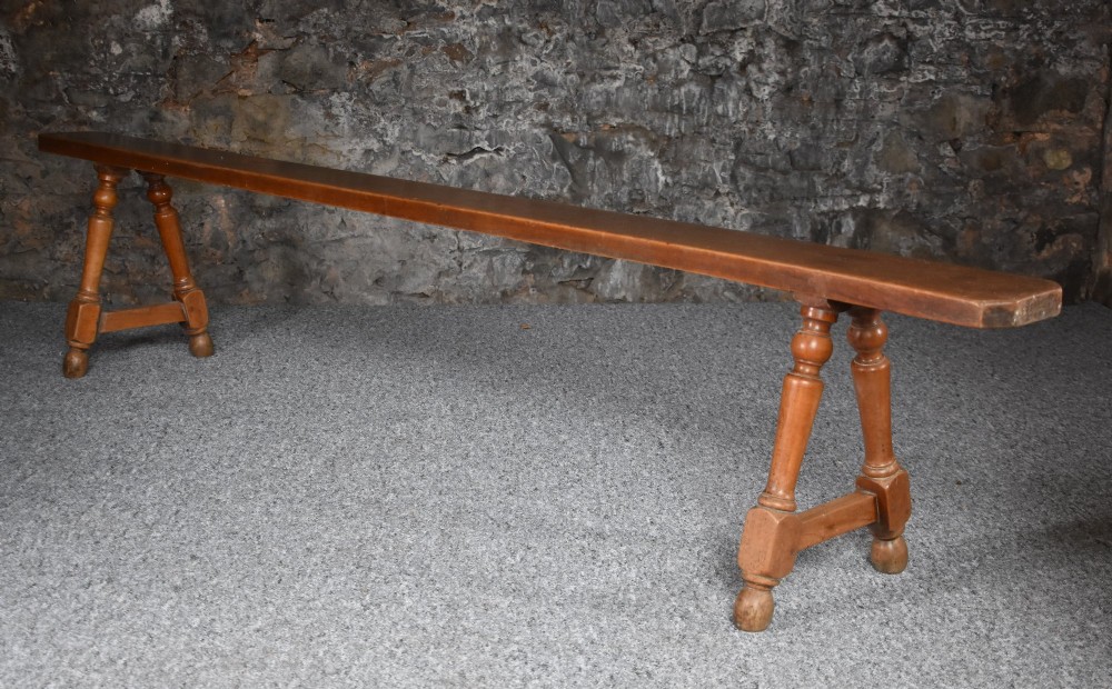 A pair of long 19th-century cherry wood benches with turned trestle legs, stretchers, and smooth timber tops. View II