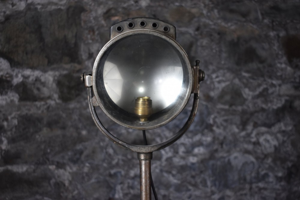 An early 20th-century Bleriot metal searchlight mounted on an adjustable dark metal telescoping floor stand with a cast tripod base. View VI