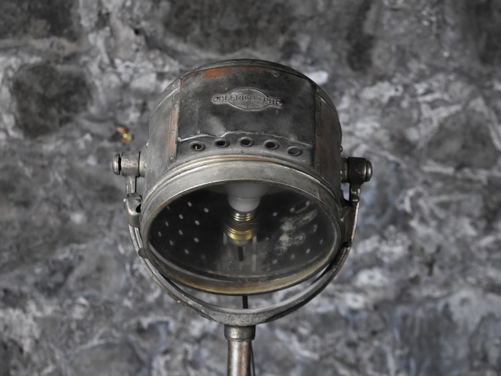 An early 20th-century Bleriot metal searchlight mounted on an adjustable dark metal telescoping floor stand with a cast tripod base. View X