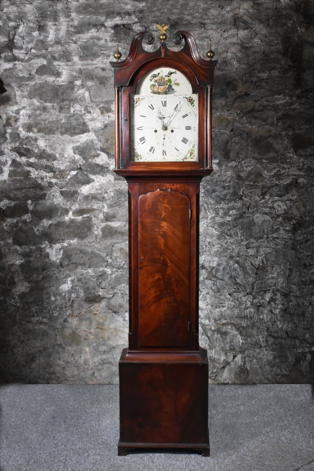 A George III flame mahogany longcase clock featuring a swan-neck pediment with brass finials and an arched painted dial with Roman numerals.