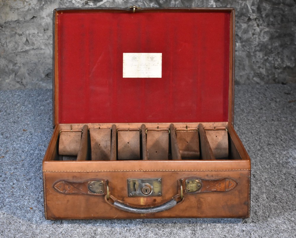 Late 19th-century tan leather cartridge case featuring an oak core, double leather straps, central brass lock, and stitched carrying handle. View V