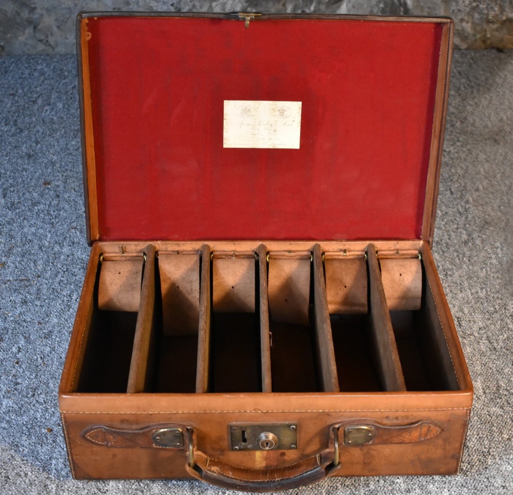 Late 19th-century tan leather cartridge case featuring an oak core, double leather straps, central brass lock, and stitched carrying handle. View VII