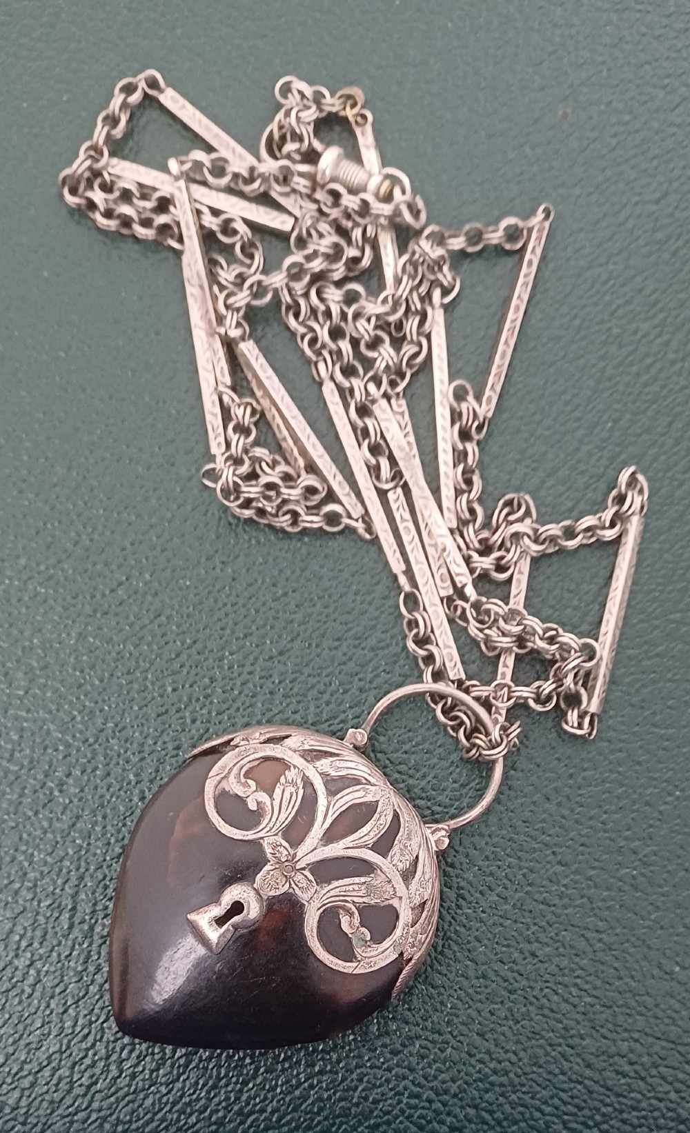 A Victorian heart-shaped tortoiseshell pendant featuring ornate silver scrollwork mounting and a keyhole motif with a top hanging loop. View V
