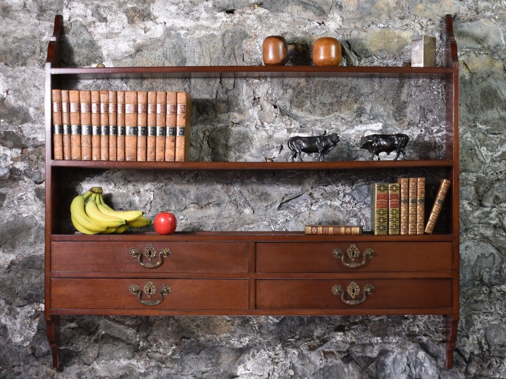 A George III mahogany wall-mounted shelf unit featuring three open display tiers set above four drawers with brass swan-neck handles.