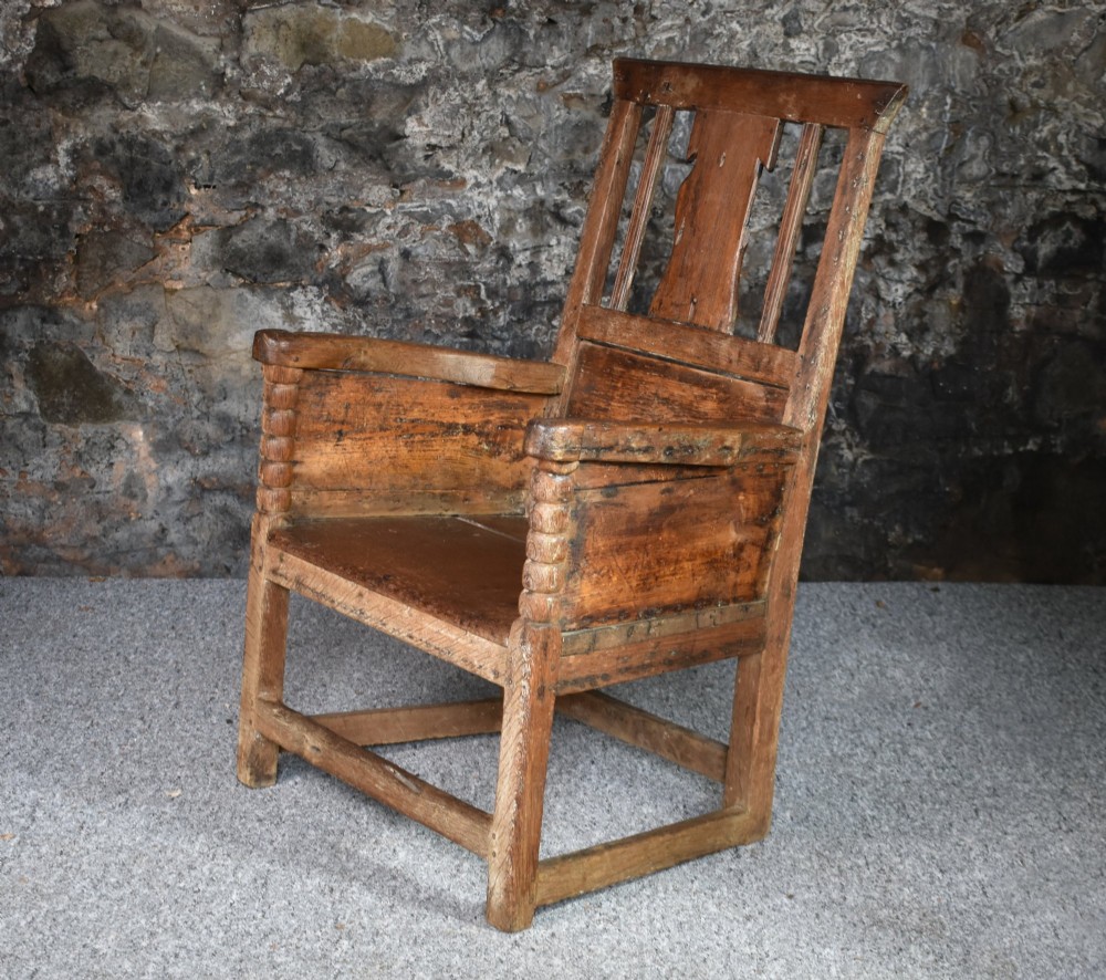 An 18th-century Scottish crofter armchair featuring turned front arm posts, panelled sides, and a slatted back in a warm wood finish.