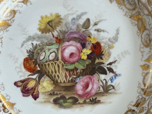 fig 1. A Regency era circular porcelain plate featuring a scalloped rim, a gold leaf foliate border, and a hand-painted central basket of colourful flowers.