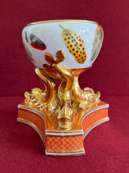 fig 1. A Regency Chamberlain Worcester porcelain pastille burner decorated with hand-painted feathers and supported by three gilt dolphin legs on a patterned orange base.