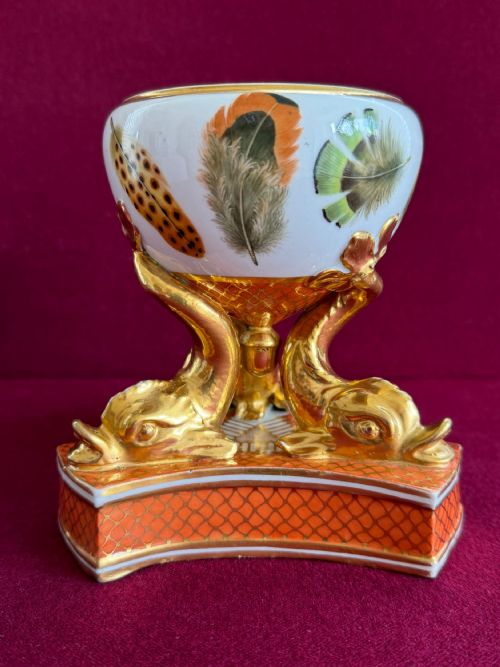 fig 2. A Regency Chamberlain Worcester porcelain pastille burner decorated with hand-painted feathers and supported by three gilt dolphin legs on a patterned orange base.