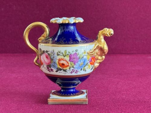 fig 1. A Regency Flight, Barr and Barr Worcester porcelain rose water sprinkler featuring a cobalt blue ground, hand-painted floral band, zoomorphic gilded spout, and loop handle on a square pedestal base.