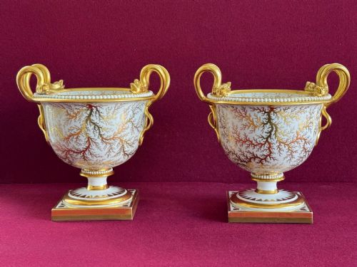 fig 1. A pair of Regency Flight, Barr and Barr Worcester porcelain urn-shaped vases featuring hand-painted figurative panels, gilded scroll handles, beaded rims, and square plinth bases.