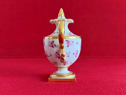 fig 1. A Regency porcelain rose water sprinkler decorated with pink painted floral sprigs, a gilded spout, a scroll handle, and a square gilded plinth base.