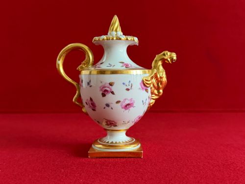 fig 2. A Regency porcelain rose water sprinkler decorated with pink painted floral sprigs, a gilded spout, a scroll handle, and a square gilded plinth base.