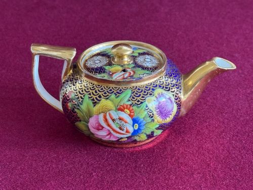 fig 1. An antique Regency period miniature porcelain teapot decorated with intricate gold scale patterns on dark blue porcelain and hand-painted floral panels.