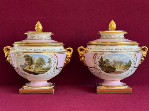 fig 2. A pair of antique Regency porcelain ice pails featuring pink and white grounds, hand-painted landscape scenes, gilded lion mask handles, and pinecone finials.