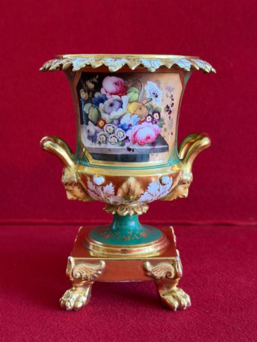 fig 1. A three-piece antique porcelain garniture set featuring green and gold gilded urns with hand-painted floral panels on pedestal bases with paw feet.