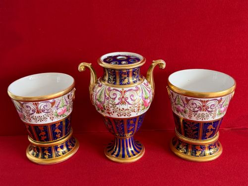 fig 1. A three-piece English Regency Spode porcelain garniture featuring a central twin-handled urn flanked by two beaker-shaped vases decorated with cobalt blue panels, hand-painted pink floral motifs, and detailed gilt scrollwork.
