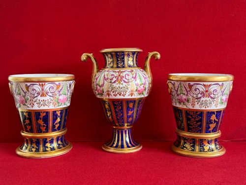fig 2. A three-piece English Regency Spode porcelain garniture featuring a central twin-handled urn flanked by two beaker-shaped vases decorated with cobalt blue panels, hand-painted pink floral motifs, and detailed gilt scrollwork.